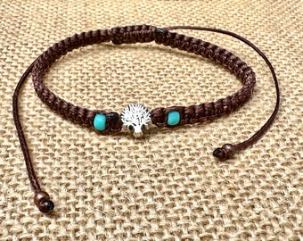 May include: A brown braided bracelet with a silver tree charm and two turquoise beads.