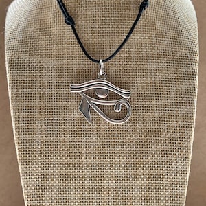 May include: A silver Eye of Horus pendant necklace on a black cord. The pendant is a detailed depiction of the ancient Egyptian symbol.