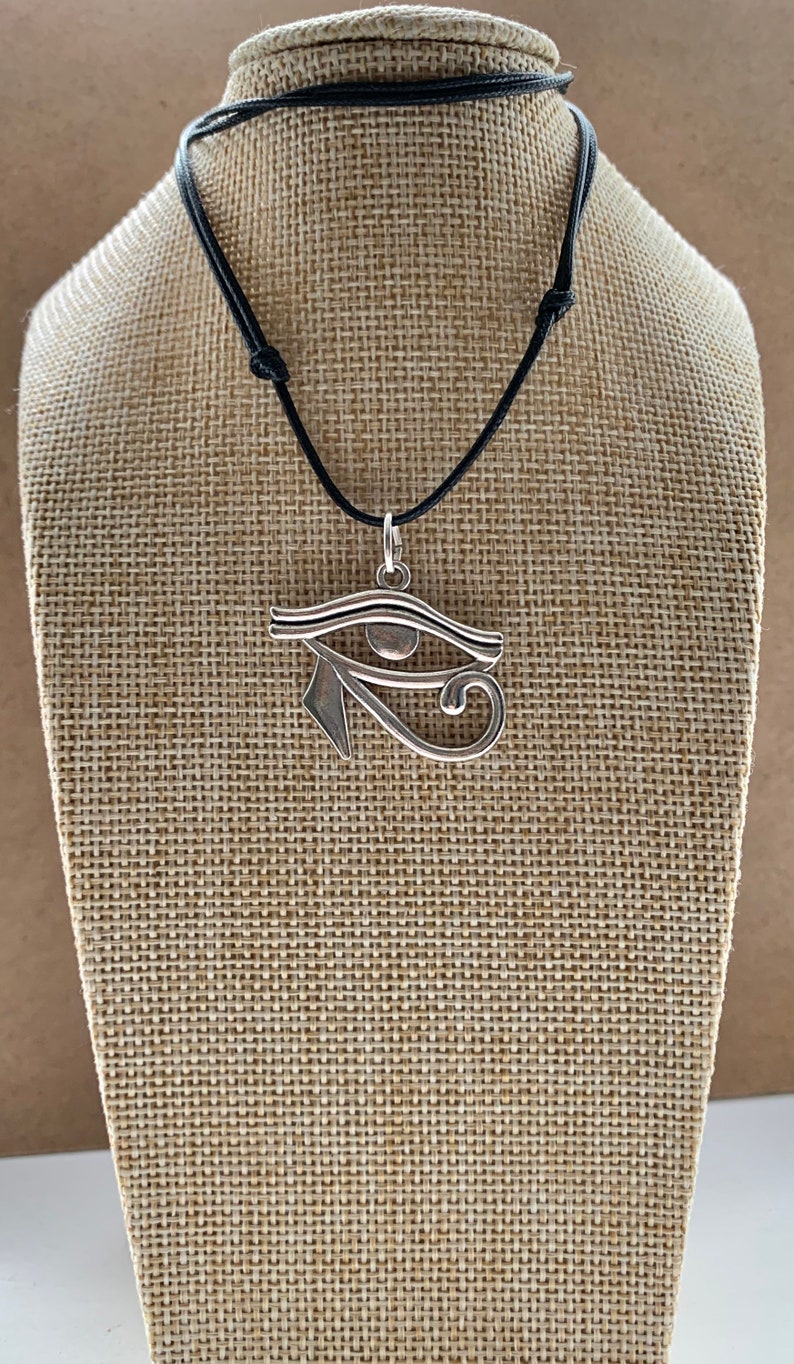 May include: A silver Eye of Horus pendant necklace on a black cord. The pendant is a detailed depiction of the ancient Egyptian symbol.