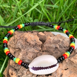 Op de afbeelding: Een zwarte kralen armband met rode, gele en groene kralen. De armband heeft een schelpbedel.