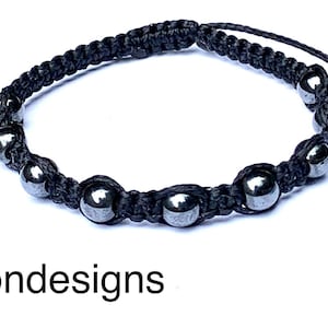 Pode incluir: Um bracelete trançado preto com contas prateadas. O bracelete tem um nó deslizante para ajustar o tamanho.