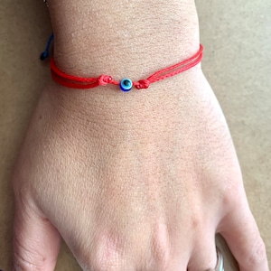 Könnte beinhalten: Rotes Armband mit einem blauen und weißen bösen Blick-Anhänger.