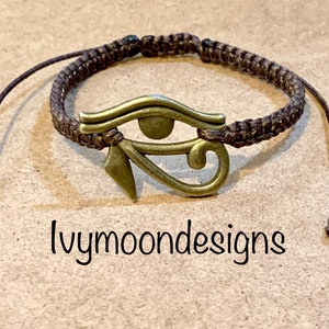 Peut inclure: Un bracelet tressé marron avec un charme œil d'Horus doré. Le charme est un symbole de protection et de bonne chance. Le bracelet est réglable et a un design simple.