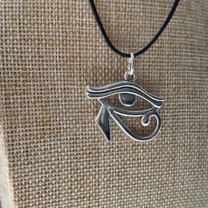May include: A silver Eye of Horus pendant necklace on a black cord. The pendant is a detailed depiction of the ancient Egyptian symbol.