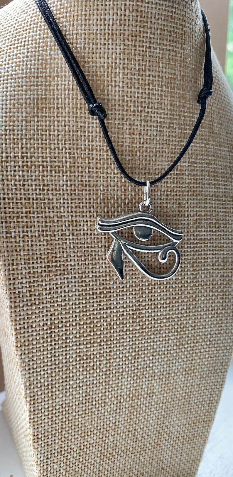 May include: A silver Eye of Horus pendant necklace on a black cord. The pendant is a detailed depiction of the ancient Egyptian symbol.