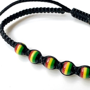 May include: A black string bracelet with five round beads. The beads are red, yellow, and green, resembling a flag.