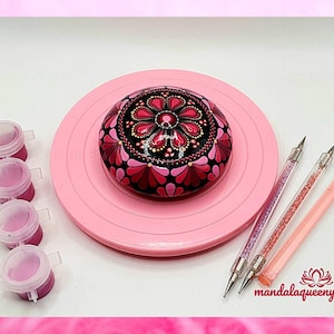Może przedstawiać: Mandala w kolorze różowym i czarnym namalowana na okrągłym kamieniu, z różowymi pojemnikami na farbę i narzędziami do kropkowania na różowej powierzchni. Tekst "mandalaqueen" jest widoczny w prawym dolnym rogu.
