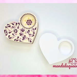 Op de afbeelding: Een witte hartvormige houten doos met een afneembaar deksel. Het deksel heeft een paars en gouden mandala-ontwerp. De doos is leeg en klaar om te worden beschilderd.