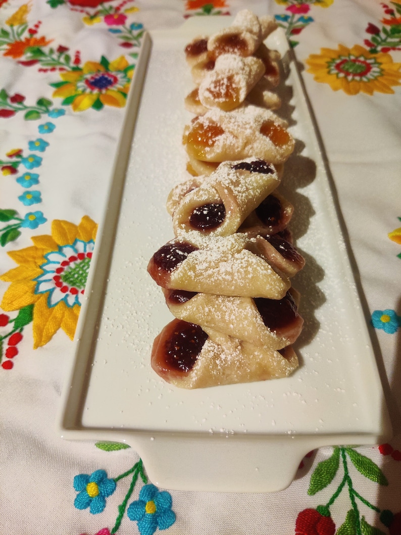 Pu&ograve; includere: Un piatto bianco con una pila di pasticcini fatti in casa. I pasticcini sono ripieni di marmellata e ricoperti di zucchero a velo.