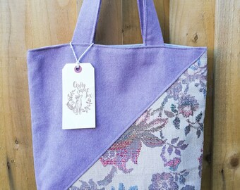 Può includere: Una borsa tote viola con un motivo floreale su un lato. La borsa ha un'etichetta che dice "Crafty Super Fox".