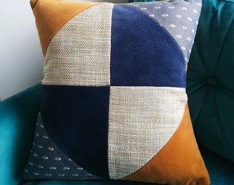 Könnte beinhalten: Ein quadratisches Kissen mit einem geometrischen Muster in Braun-, Beige-, Marineblau- und Grautönen. Das Kissen besteht aus verschiedenen Stoffen, darunter Samt und ein strukturierter Stoff.