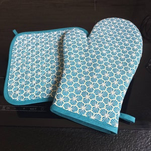 Peut inclure: Deux maniques de four bleu turquoise avec un motif géométrique d'étoiles blanches et jaunes. Les maniques sont en tissu matelassé et ont une boucle de suspension.