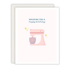 May include: A greeting card with a light pink background and a white border. The card features a pink stand mixer illustration with the text "Whisking you a happy birthday" in blue script. Yellow starbursts accent the mixer.