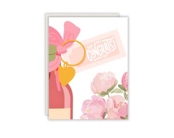 Könnte beinhalten: Eine Grußkarte mit einer Aquarellillustration einer rosafarbenen Flasche mit einer großen rosa Schleife, einem goldenen herzförmigen Anhänger und einem Etikett mit dem weißen Schriftzug CONGRATS!. Unten rechts befindet sich ein Strauß rosa Pfingstrosen.