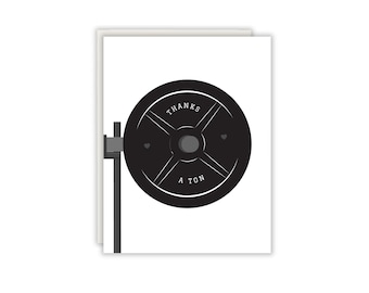 Könnte beinhalten: Eine weiße Grußkarte mit einer Illustration einer schwarzen Hantelscheibe auf einer grauen Hantelstangenaufnahme. Die Hantelscheibe trägt den weißen Schriftzug THANKS A TON sowie zwei kleine Herzsymbole auf der schwarzen Oberfläche.