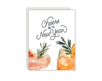 Könnte beinhalten: Eine weiße Grußkarte mit dem dunkelgrauen kursiven Text Cheers to a New Year über zwei Aquarellillustrationen von Cocktails. Ein Glas enthält ein rosa Getränk mit einer Grapefruitscheibe und Rosmarin, das andere ein orangefarbenes Getränk.