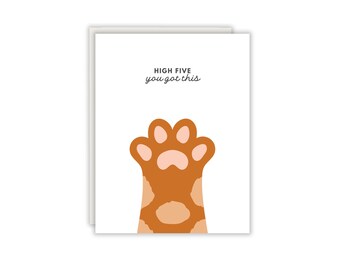Könnte beinhalten: Eine weiße Grußkarte mit einer grafischen Illustration einer orangefarbenen Katzenpfote mit hellrosa Ballen. Der Text "HIGH FIVE you got this" ist in Schwarz über der Pfote gedruckt. Die Karte wird mit einem passenden weißen Umschlag gezeigt.