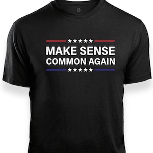 以下が含まれることがあります： 胸の中央に白い文字で「MAKE SENSE COMMON AGAIN」とプリントされた黒い半袖Tシャツ。テキストの上には5つの白い星が並んだ赤い水平線、下には5つの白い星が並んだ青い水平線が配置されています。