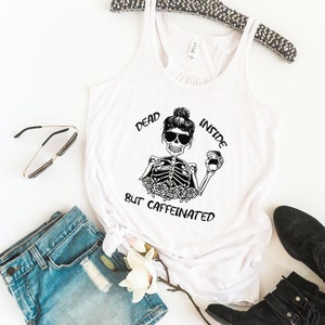 May include: White tank top with a black and white graphic of a skeleton holding a coffee cup. The text on the graphic reads "Dead Inside But Caffeinated".