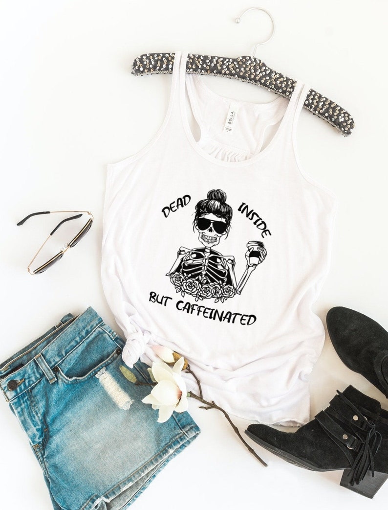May include: White tank top with a black and white graphic of a skeleton holding a coffee cup. The text on the graphic reads "Dead Inside But Caffeinated".