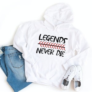 May include: White hooded sweatshirt with the text "Legends Never Die" in black lettering. A red and black baseball stitch graphic is above the text.