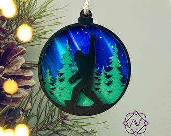May include: A round wooden Christmas ornament with a silhouette of Bigfoot standing in a forest with a starry night sky background.