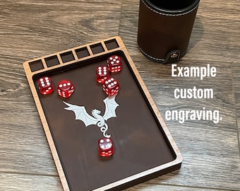 May include: A wooden dice tray with a dragon design engraved on the surface. The tray has compartments for dice and is shown with red dice. The text "Example custom engraving." is visible in the image.