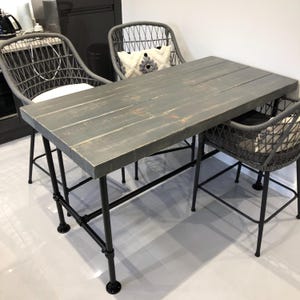 May include: A gray wooden table with black metal legs and two gray wicker chairs. The table has a rustic, farmhouse style.