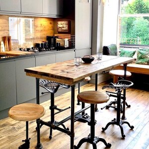 May include: A rustic kitchen island with a reclaimed wood tabletop and black metal pipe legs. The island is paired with adjustable stools with wooden seats and cast iron bases. Overhead, clear glass pendant lights illuminate the space.