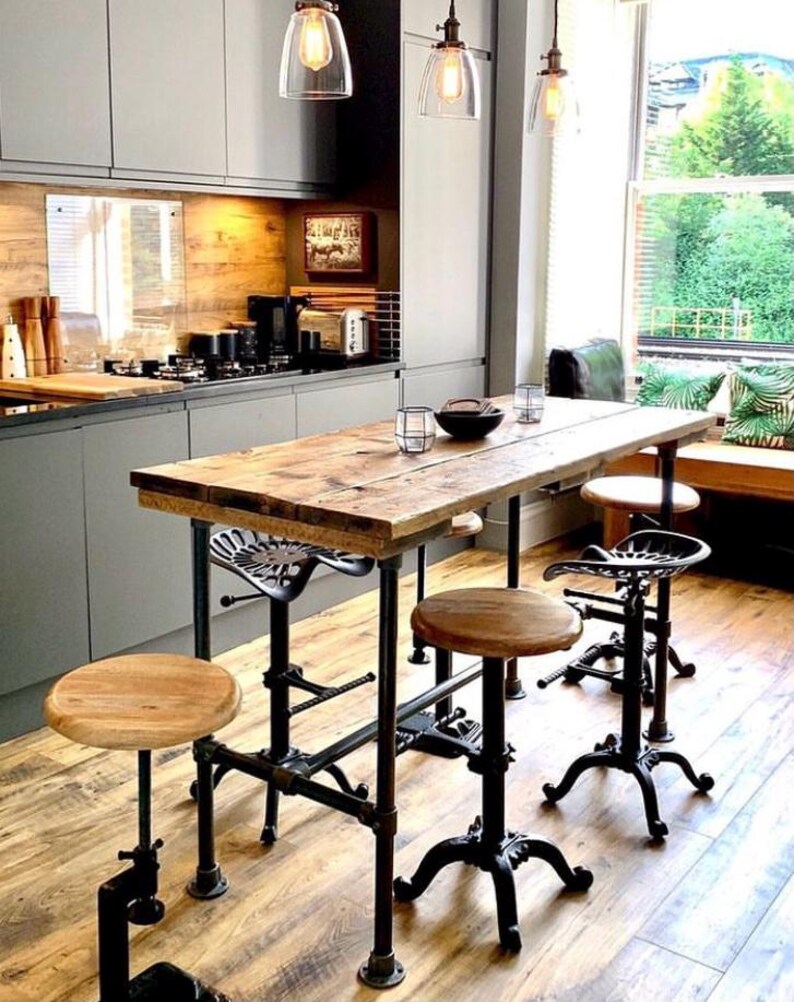May include: A rustic kitchen island with a reclaimed wood tabletop and black metal pipe legs. The island is paired with adjustable stools with wooden seats and cast iron bases. Overhead, clear glass pendant lights illuminate the space.