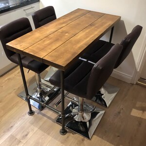 May include: A wooden rectangular table with a brown finish, supported by a black metal frame. Four brown leather bar stools with chrome bases are positioned around the table. The table measures approximately 48 inches long.
