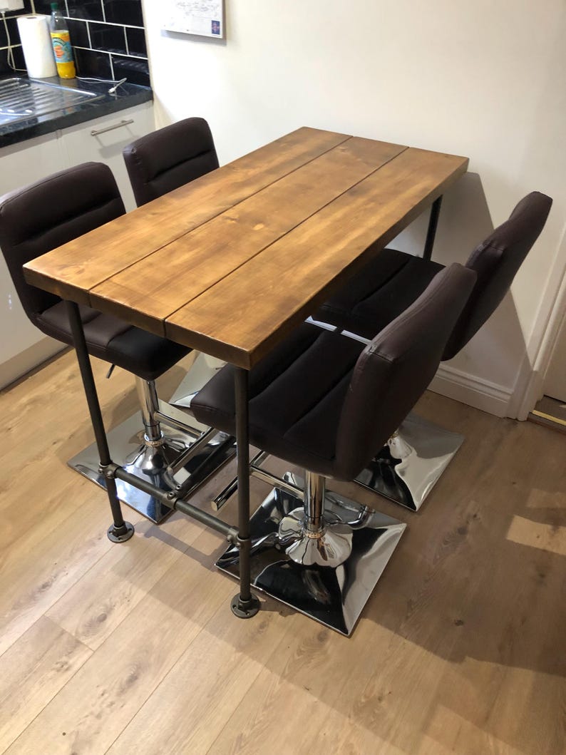 May include: A wooden rectangular table with a brown finish, supported by a black metal frame. Four brown leather bar stools with chrome bases are positioned around the table. The table measures approximately 48 inches long.