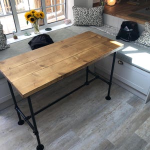 May include: A rectangular wooden table with a light brown finish. The tabletop is supported by black metal pipe legs. The table is approximately 60 inches long and 30 inches wide. The table is suitable for a kitchen or dining area.