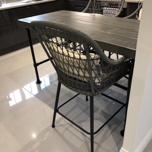 May include: A black wooden table with a black metal frame and two gray rope chairs with white cushions. The chairs have a black metal frame and a gray rope seat and back.