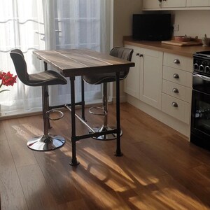 May include: A rustic kitchen island with a dark wood tabletop and black metal pipe legs. Two gray upholstered bar stools with chrome bases are positioned at the island. The island is in front of a window with sheer curtains.