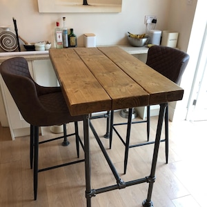 May include: A rustic wooden bar table with a black metal frame. The table has a natural wood finish and is supported by four black metal legs. Two brown leather bar stools are placed at the table.