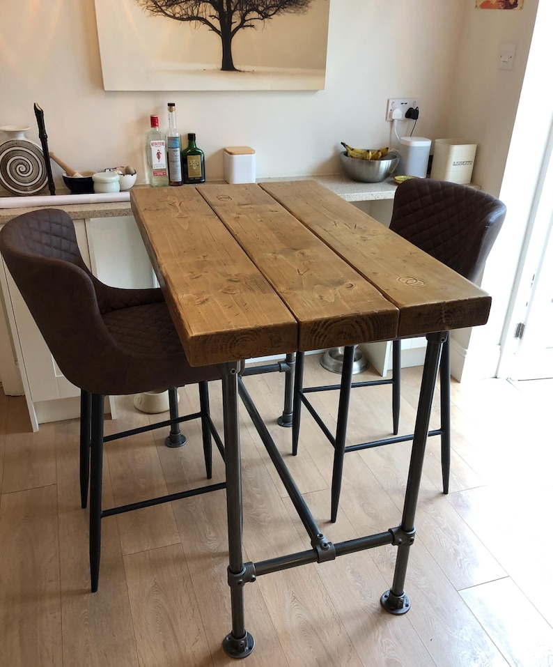 May include: A rustic wooden bar table with a black metal frame. The table has a natural wood finish and is supported by four black metal legs. Two brown leather bar stools are placed at the table.