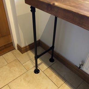 May include: A rustic wooden table with black metal pipe legs. The table is made of reclaimed wood and has a natural finish. The legs are made of industrial pipe and have a black powder coat finish.