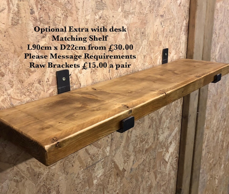 May include: A wooden shelf, approximately 35 inches long and 8.7 inches deep, mounted on black metal brackets. The shelf has a natural wood grain finish and is attached to a light brown wall. Text on the wall reads "Optional Extra with desk Matching Shelf".