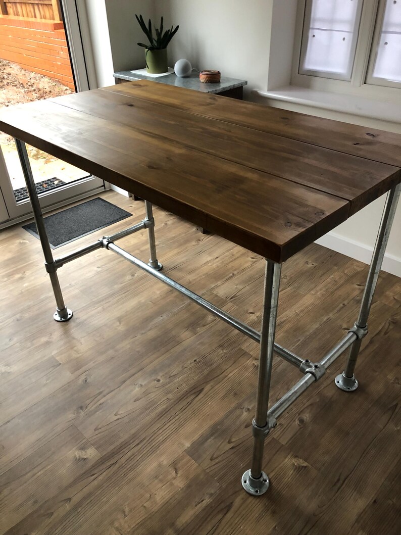 May include: A rectangular wooden table with a dark brown finish. The table is supported by galvanized steel pipes and fittings. The table has a rustic, industrial design and is suitable for various uses.