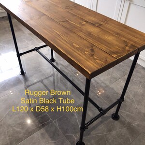 May include: A rectangular table with a Rugger Brown wooden top and black metal pipe legs. The table measures 47.2 inches long, 22.8 inches wide, and 39.4 inches high. The text on the image reads "Rugger Brown Satin Black Tube L120 x D58 x H100cm."