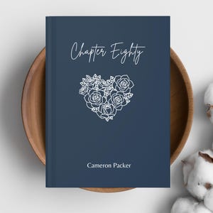 Puede incluir: Una cubierta de libro azul marino con las palabras "Chapter Eighty" en cursiva sobre un diseño floral en forma de corazón. El nombre del autor, "Cameron Packer", está impreso debajo.