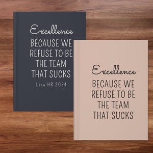 May include: Two notebooks with the text "Excellence BECAUSE WE REFUSE TO BE THE TEAM THAT SUCKS". One notebook is dark blue, the other is light pink. The dark blue notebook has "Lina HR 2024" printed on it.