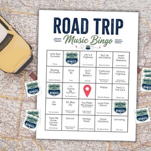 May include: A yellow toy car sits on a map beside a "Road Trip Music Bingo" game sheet. The bingo card features song titles and a red location marker. Several "Road Trip Bingo" stickers are scattered around the game.
