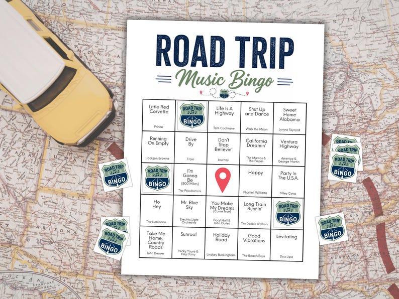 May include: A yellow toy car sits on a map beside a "Road Trip Music Bingo" game sheet. The bingo card features song titles and a red location marker. Several "Road Trip Bingo" stickers are scattered around the game.