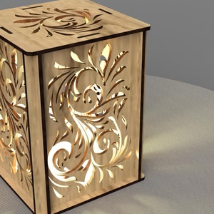 May include: A wooden lamp with a decorative floral design cut out of the sides. The lamp is lit and casting a warm glow.