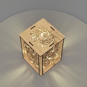 May include: A wooden lamp with a decorative cutout design on all sides. The lamp is lit and casting a warm glow.