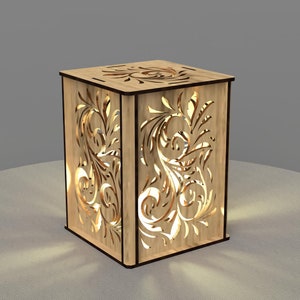 May include: A wooden lamp with a decorative floral design cut out of the sides. The lamp is lit and casting a warm glow.