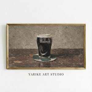 May include: A framed print of a pint of Guinness stout on a green coaster. The glass is filled with dark beer and has the Guinness logo. The artwork is set on a wooden table with a neutral background. The text "YARIKE ART STUDIO" is at the bottom.