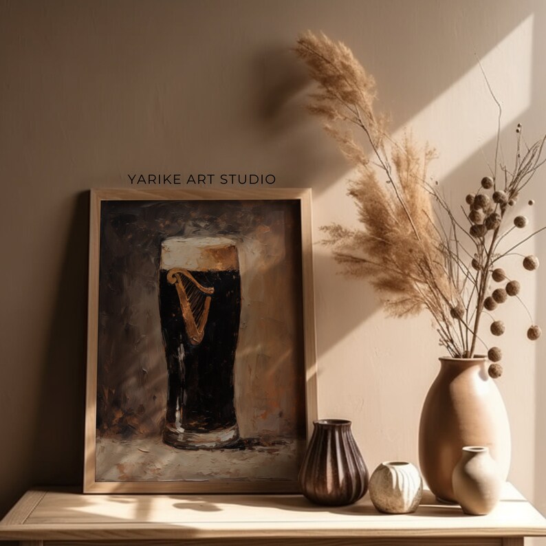 May include: A framed painting depicting a glass of dark beer with a white head. The beer features a gold harp logo. The painting is displayed on a wooden table with a vase of dried flowers and other decorative items.